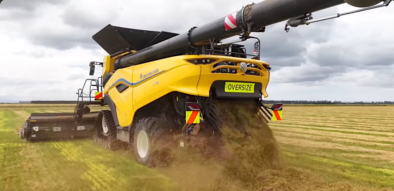 New Zealand harvester with their mandated hazard panels, oversize sign and E.U.-style boom stripes. Illustrative, demonstrative screenshot from online video.